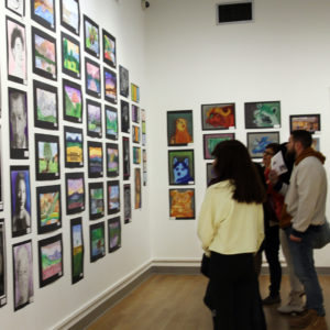 A group of people admiring a wall of student art that almost reaches the ceiling