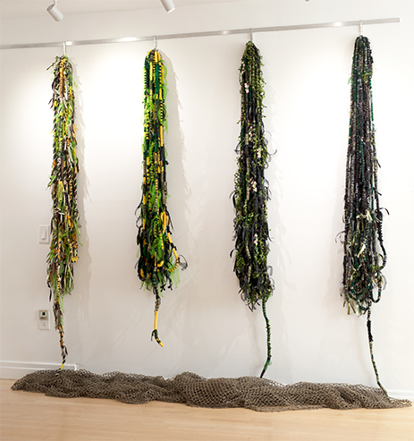Four representations of hair made of cotton rope wrapped in yarn, material, recycled sari thread, and ribbons hang from a wall in a gallery