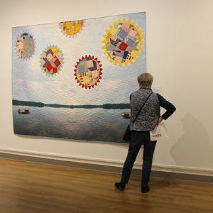 A woman examining an art quilt that shows a landscape with multicolored ball in the sky