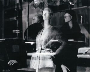A reflection almost obscures the three mannequins in an image of a storefront window