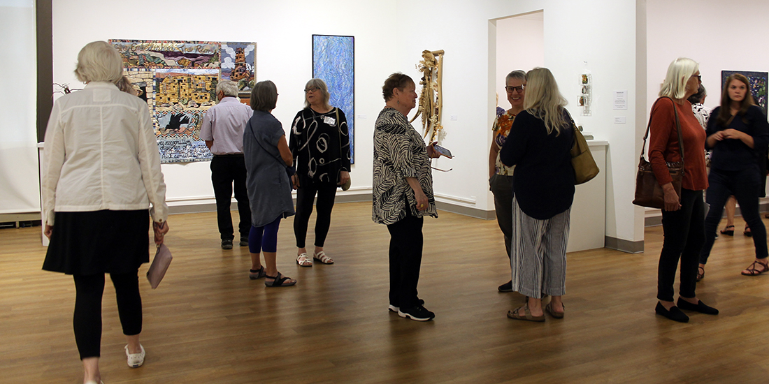 A group of people milling about a gallery, looking at the artwork or talkiing in small groups