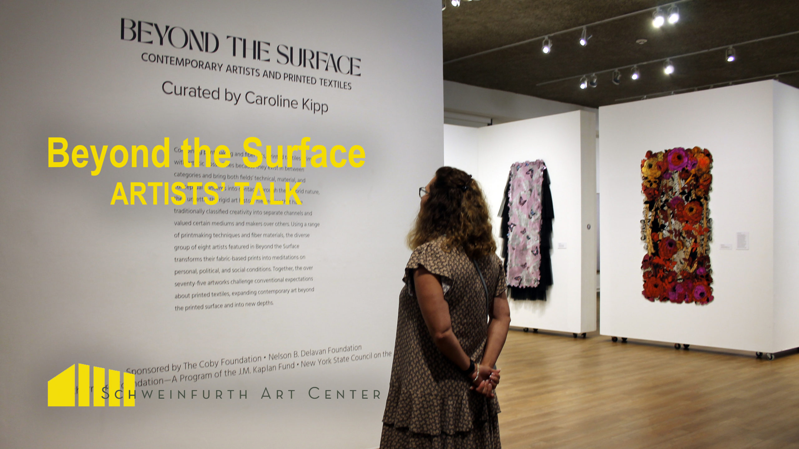 A woman reads the introduction to the "Beyond the Surface" description on a white wall at the Schweinfurth Art Center in Auburn NY