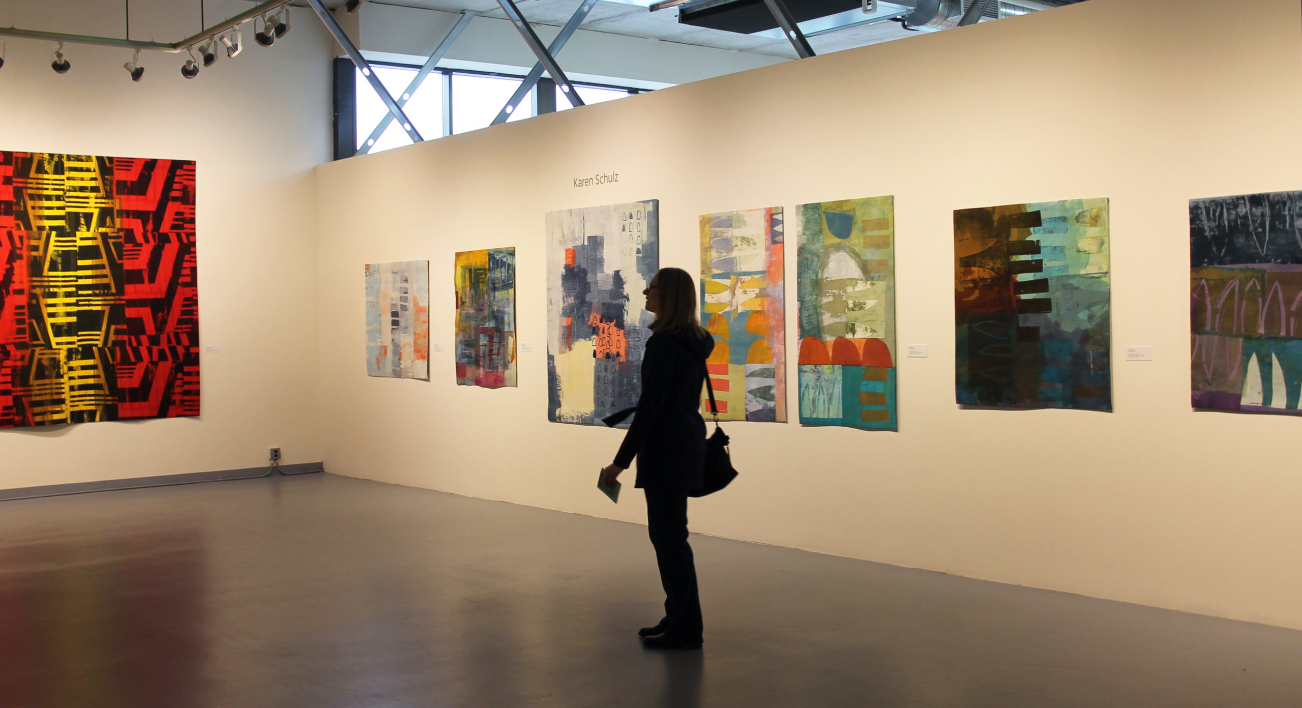 A sihoutted woman stands in a gallery filled with brightly colored art quilts