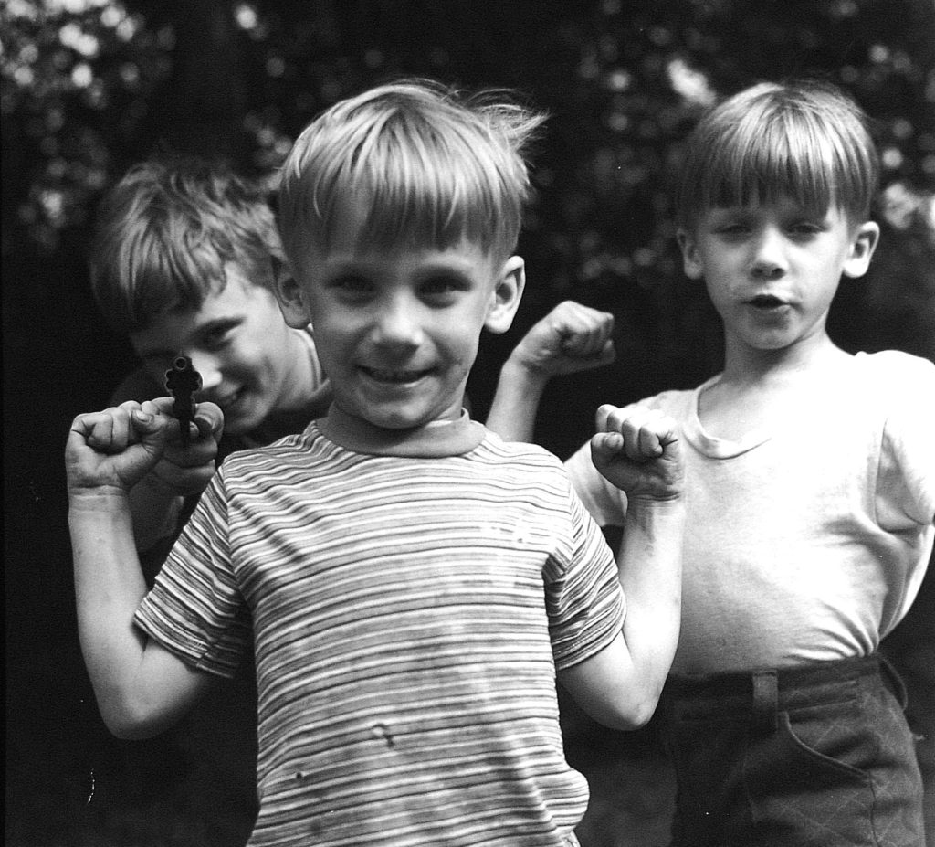Black and white photo of three boys, one holsing a toy pistol aimed at the camera